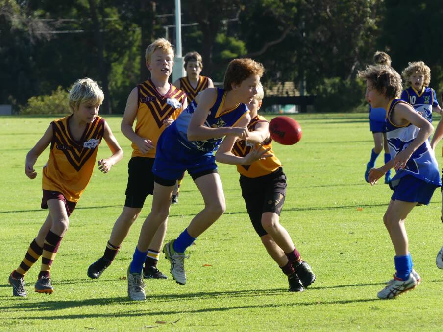 Seb Royal gets a handpass away for Hawks Blue despite fierce attention from Avion Packer and Kai Luttrell in the 11s game at Cowaramup.