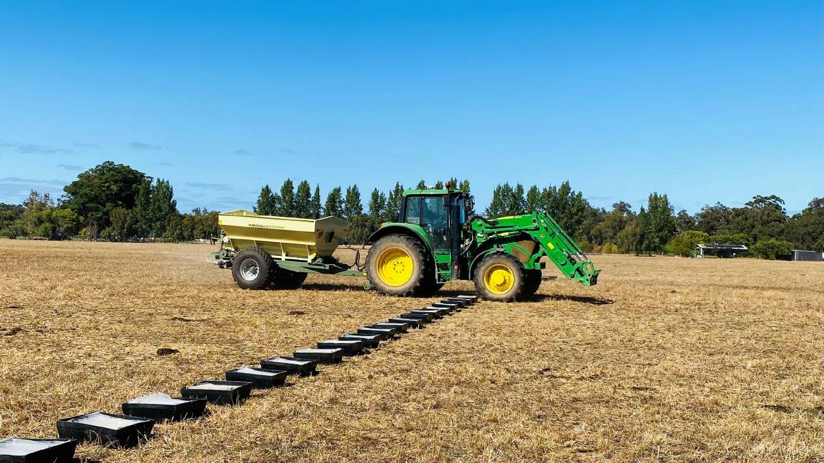 A tractor and fertiliser spreader run through the paddock. Fertiliser is caught in trays laid out and measured to determine the spread pattern.